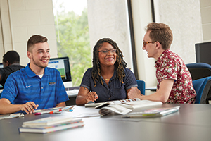 three journalism students talking and working around table
