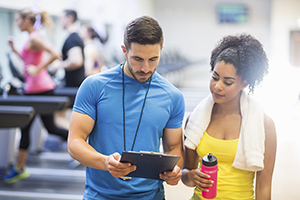 personal trainer showing clipboard to female with towel around her neck