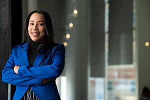 female student wearing blue suit jacket leaned against glass wall
