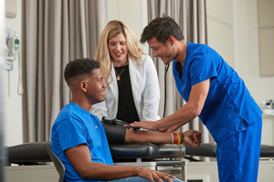 professor guiding student through taking blood pressure of another student