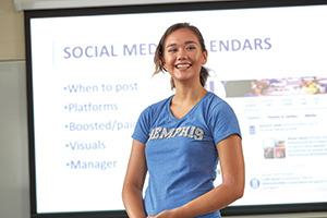 student presenting to class with "social media" powerpoint in background