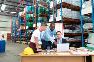 three people looking at a laptop in a warehouse